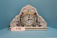 Full front view of white ceramic clock holder with round clock face surrounded by floral decoration