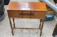 Front view of closed wooden sewing stand with two hinged covers and three drawers.