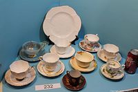 Full lot view of tea cups and saucers including Shelley cup and plate with a soda can for scale