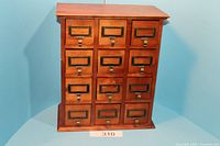 Front view of small wooden drawer unit with 12 drawers, showing the cabinet shape and metal label holders attached to each drawer.
