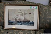 Framed print showing the sailing ship Spinaway in full sail on the ocean with sky and water in background, placed on a patterned couch.