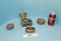 Four assorted decorative trinket boxes arranged with a soda can for scale.