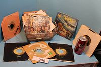 Photo showing a basket filled with various vintage 45 RPM records in paper sleeves plus a Star Wars themed record with Chewbacca on cover and a Dr. Pepper can for scale.