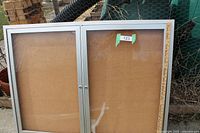 Wall hanging showcase cabinet front view, showing silver metal frame, double glass doors, one broken pane, and placard with number 123.