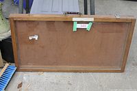 Wooden framed rectangular glass showcase laid face down on the ground showing the wooden back panel, handle, and latch hardware.