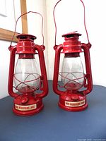Pair of red American Camper kerosene lamps front view showing glass globes and handles