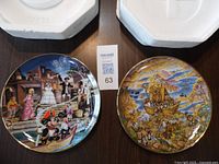 Two decorative collector plates side by side on white wrapping, showing full front designs.