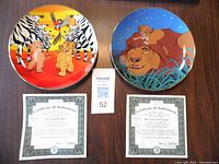Two Bradford Exchange plates from The Lion King Circle of Life series with certificates of authenticity placed below each plate on a wood surface.
