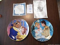 Two Bradford Exchange Disney collectible plates with accompanying certificate and paperwork shown on table