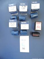 Six hole saws and their boxes laid out on a flat surface, including five blue Blu-Mol units and one black Simonds unit, all appear unused with original packaging.