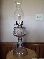 Full assembled view of the kerosene lamp showing the clear embossed glass body, brass wick turner, and chimney.