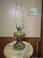 Antique green glass kerosene lamp fully assembled on a wooden surface, showing height and general shape.