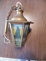Side view of antique hanging light fixture showing painted tree design in six glass panels and metal frame with chain.