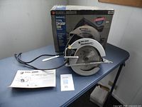 Photo shows the Black & Decker SawForce 7 1/4 inch circular saw on a table with its power cord, instruction manual, and the original box in the background.
