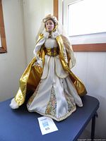 Full view of the 1989 Danbury Mint Queen Guinevere doll wearing a cream and gold gown with floral inserts, standing 20 inches tall.
