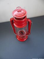 Front angle view of red DIETZ American Camper RK12 kerosene lantern showing top lid with embossed DIETZ logo and glass chimney with wick and metal frame.