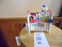Angle showing the Enesco Disney crib musical figurine with characters Mickey, Minnie, and Donald on a small table.