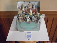 View of the open music box showing various detailed porcelain figurines and miniatures arranged inside the case.