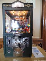 Front view of the Enesco The Grabber coin-operated toy claw machine showing glass display with small toys inside, coin slot, push/pull lever, and decorative details.