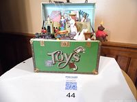 Front view of green Enesco music box labeled 'Toys' with miniature toys inside including a marionette clown and a man with umbrella