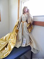 Front view of Queen Galadriel porcelain doll standing on a surface near a window, showing the detailed gown and golden cape.