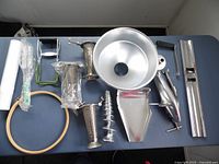 All metal components of Garden Way's Original Squeezo Strainer model 09142 spread on table showing funnel, crank, auger, and attachments.