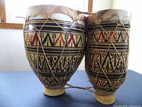 Front view of two ceramic bongos showing colorful geometric painted patterns and natural rawhide drumheads held by rope tensioning.