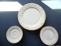 Top view of three plates: a large dinner plate, a medium salad plate, and a small bread-and-butter plate with gold rims and floral pattern on white china.