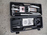 Rally hydraulic floor jack placed inside its black plastic carrying case alongside the handle and instruction manual.