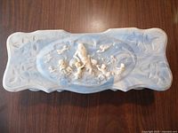 Top view of the light blue Incolay stone trinket box showing the detailed carved cherubs on the lid framed by floral motifs and scalloped edges.