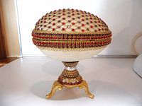 Front view of vintage handcrafted rhinestone egg with red rhinestones and gold detailing on a tripod stand.