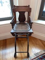 Front view of the antique oak child's high chair showing carved press back design, cane seat, and front wheels.