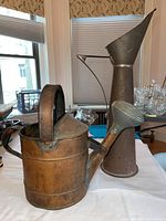Copper watering can and tall metal watering pitcher side by side on table by window under natural light