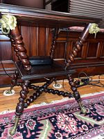 Full view of antique wooden side table with twisted legs, bottom shelf, and brass claw feet resting on a patterned rug.