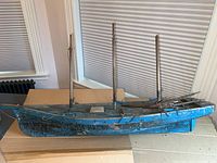 Front side view of the antique wooden boat showing its blue painted hull, three masts, and overall wear.