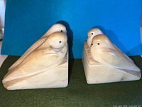 Front and side view of the pair of symmetrical marble bookends depicting budgie birds in Egyptian revival style, showing natural marble tones and slight wear.