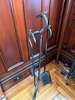 Full view of the metal fireplace tools set including shovel, poker, and tongs with bird head handles standing in the matching metal stand.