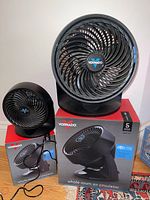 Two Vornado black whole room air circulator fans on top of their original boxes, showing front grill and logo clearly.