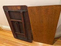 Photo shows the reverse side of one folding table with legs folded against the underside of the wooden tabletop.
