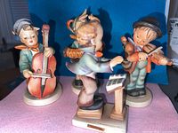 Four Hummel musical figurines arranged together including band leader, cellist, accordion player, and violinist.