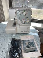White Pfaff Hobbylock 4752 serger sewing machine with instruction manual and black power cord on a table with white lace cloth.