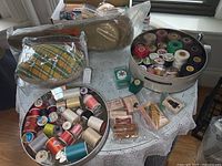 Wide view of lot showing spools of thread in round tins, craft stamps with ink pads, and vintage sleeve board on a white tablecloth.
