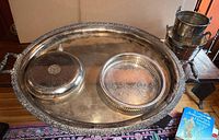 Oval silver plated tray with two hot water bottles, a round silver tray, and stacked bucket and cup on a rug