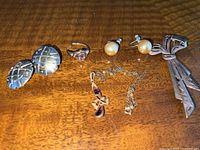 All five items arranged on wood surface: brooch, earrings, cufflinks, ring, pendant