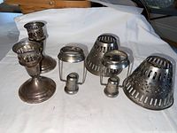 Front view of two weighted sterling candle holder bases with three decorative openwork tops detached and placed beside them on white background.