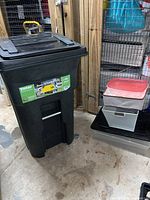 Wide angle view of the Toter trash tote alongside stacked plastic storage bins with lids.