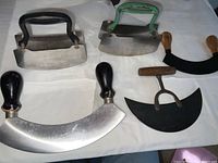 Top-down image of five vintage kitchen choppers arranged on white cloth showing different handles and blade shapes.