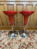 Pair of red vintage swivel bar stools with chrome pedestal bases placed on floral carpet with wood panel background.