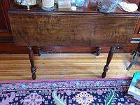 Front view of wooden drop leaf table showing closed leaf and turned legs on hardwood floor.
