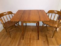 Full view of wooden drop leaf table with two vintage wooden chairs on each side, showing wood floor background.